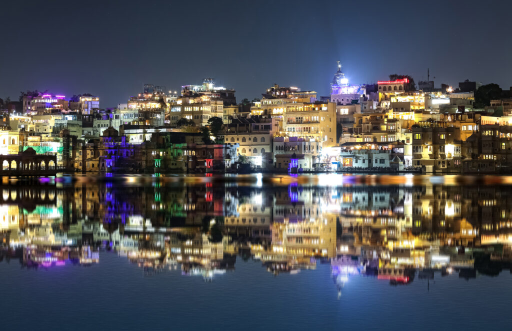 インド、ラージャスターン州ウダイプールのピチョーラ湖に水が反射するウダイプールの夜の街並み